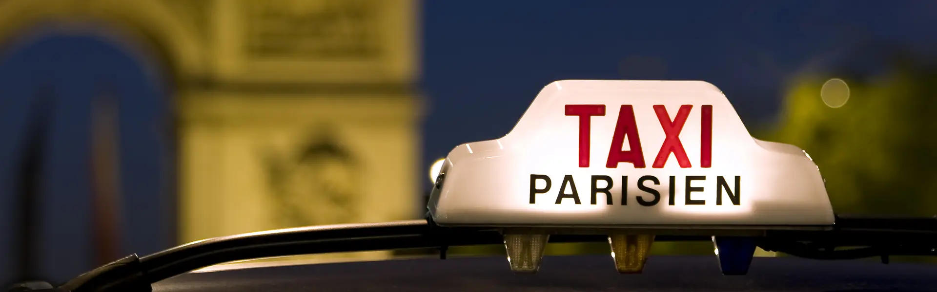 Taxi-Dachzeichen mit der Aufschrift 'TAXI PARISIEN' vor einem unscharfen Hintergrund