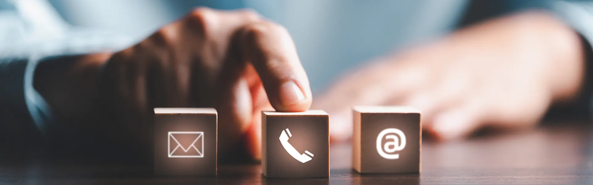  A hand points to a die with a telephone symbol, while two other dice with an email symbol and an @ symbol lie next to it